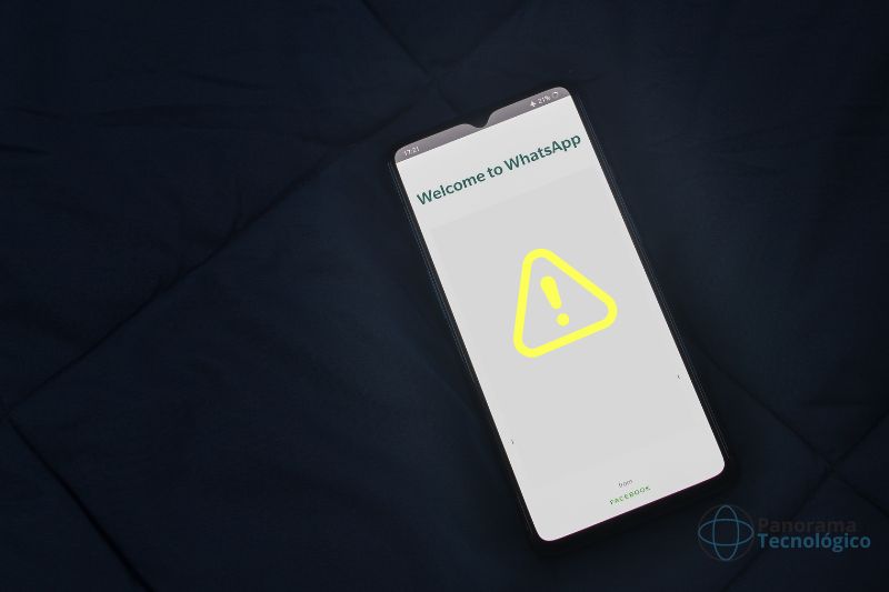 Smartphone mostrando tela inicial do WhatsApp com um símbolo de exclamação indicando problemas no serviço. O aparelho está sobre um tecido na cor azul escuro