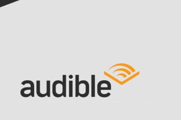 Banner divulgação do serviço Amazon Audible, o serviço de audiolivros da Amazon. No banner, um fone cobrindo uma pilha de livros coloridos e o logotipo do serviço