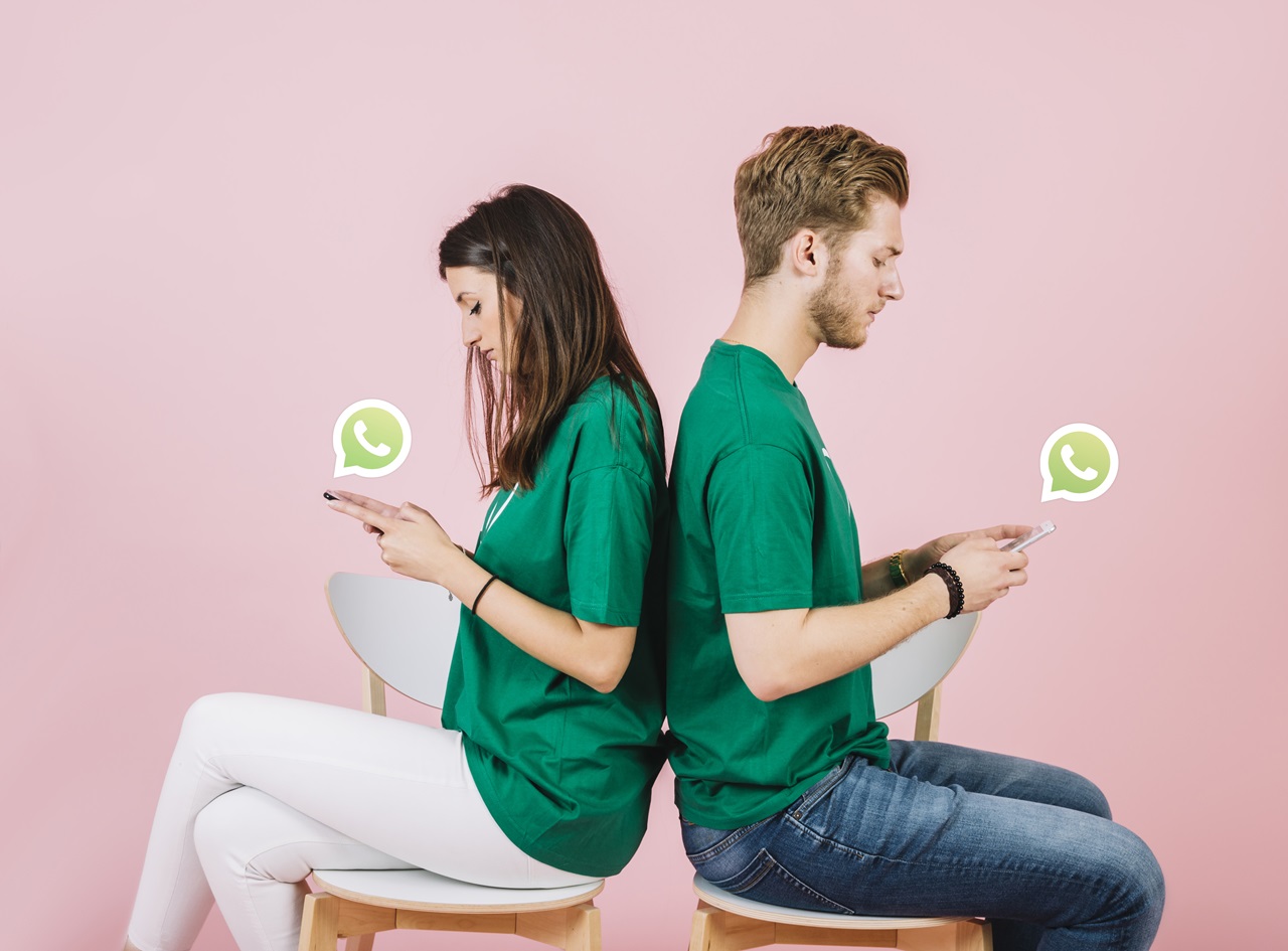Jovem casal sentado de costas usando o WhatsApp. Imagem de Freepik.