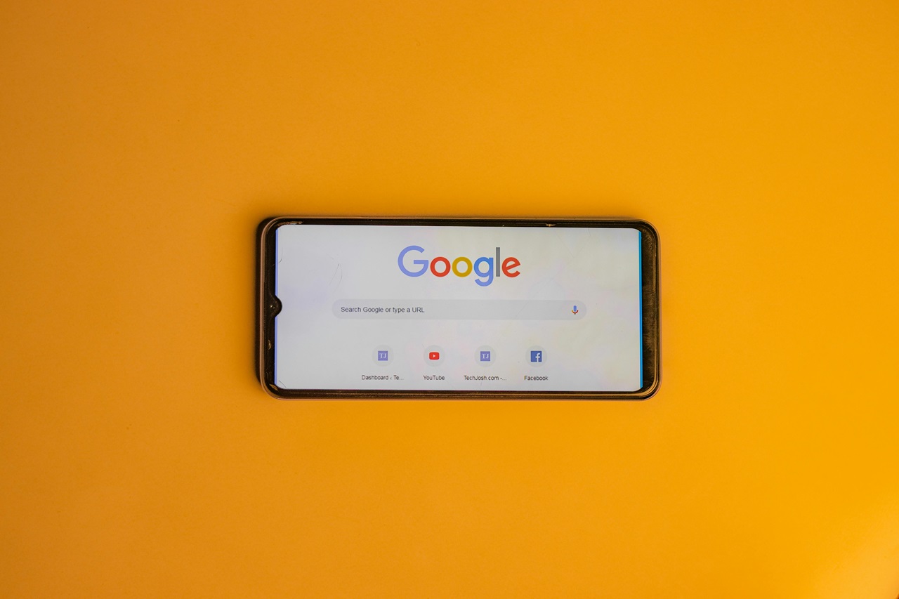 Smartphone sobre uma superfície laranja, exibindo a página inicial do Google com o logotipo e a barra de pesquisa. Imagem: Shantanu Kumar / PExels