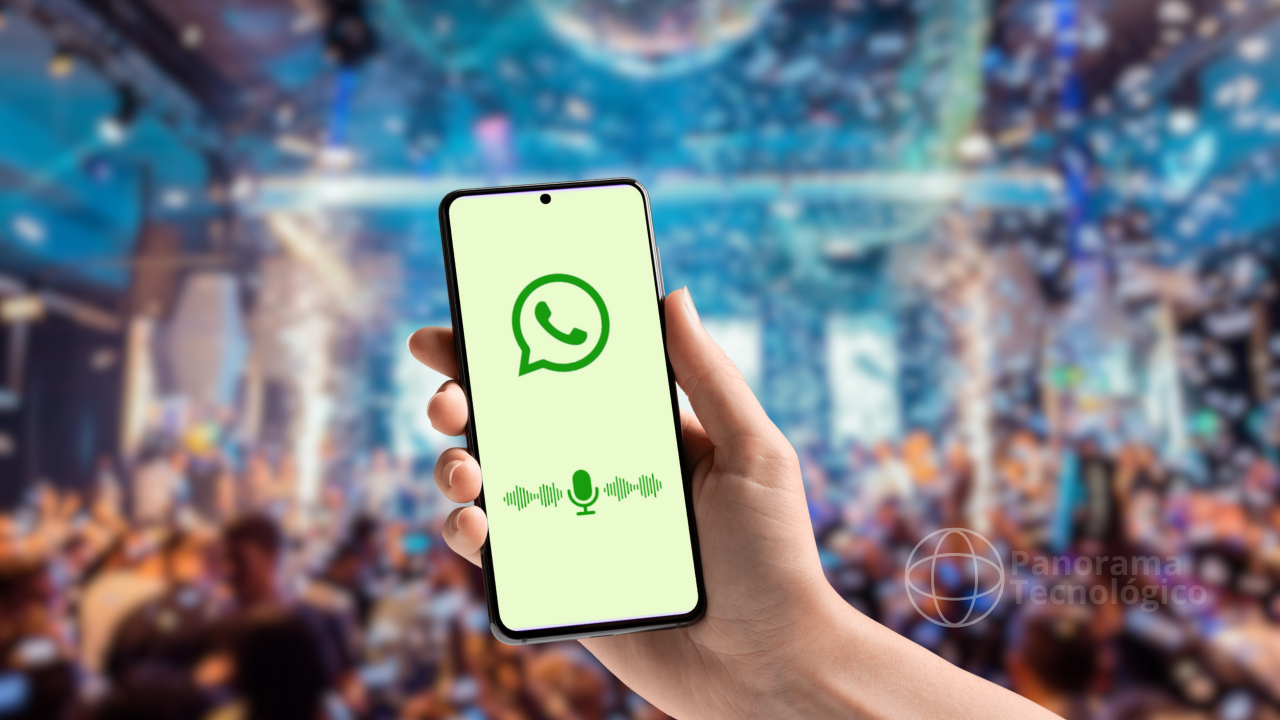 Imagem mostrando uma mão segurando um smartphone com a tela exibindo o logotipo do WhatsApp e um ícone de microfone com ondas sonoras, indicando a funcionalidade de transcrição de mensagens de áudio em texto. O fundo está desfocado, sugerindo um ambiente de festa ou evento com muitas pessoas e luzes coloridas. No canto inferior direito, há um logotipo com o texto 'Panorama Tecnológico'. A imagem destaca uma nova funcionalidade do WhatsApp que facilita a comunicação em ambientes barulhentos ou para pessoas com deficiência auditiva. Imagem: ilustração Panorama Tecnológico.