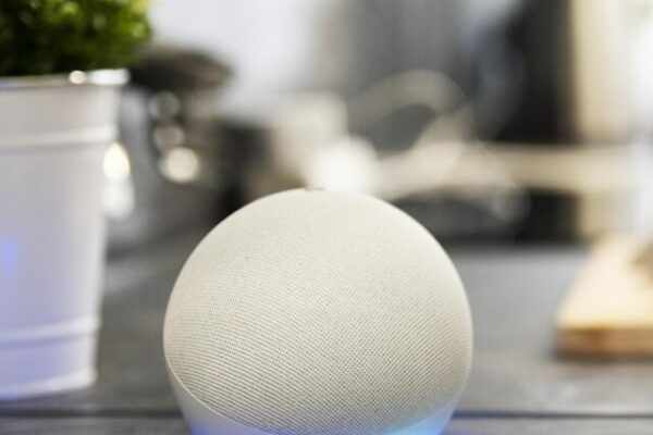 A imagem mostra uma as mãos de uma pessoa cortando legumes em cima de uma bancada de uma cozinha. A imagem está um pouco desfocada e mostra um vaso de planta e um dispositivo Echo Dot 5ª geração com Alexa na cor branca. Imagem de Freepik.