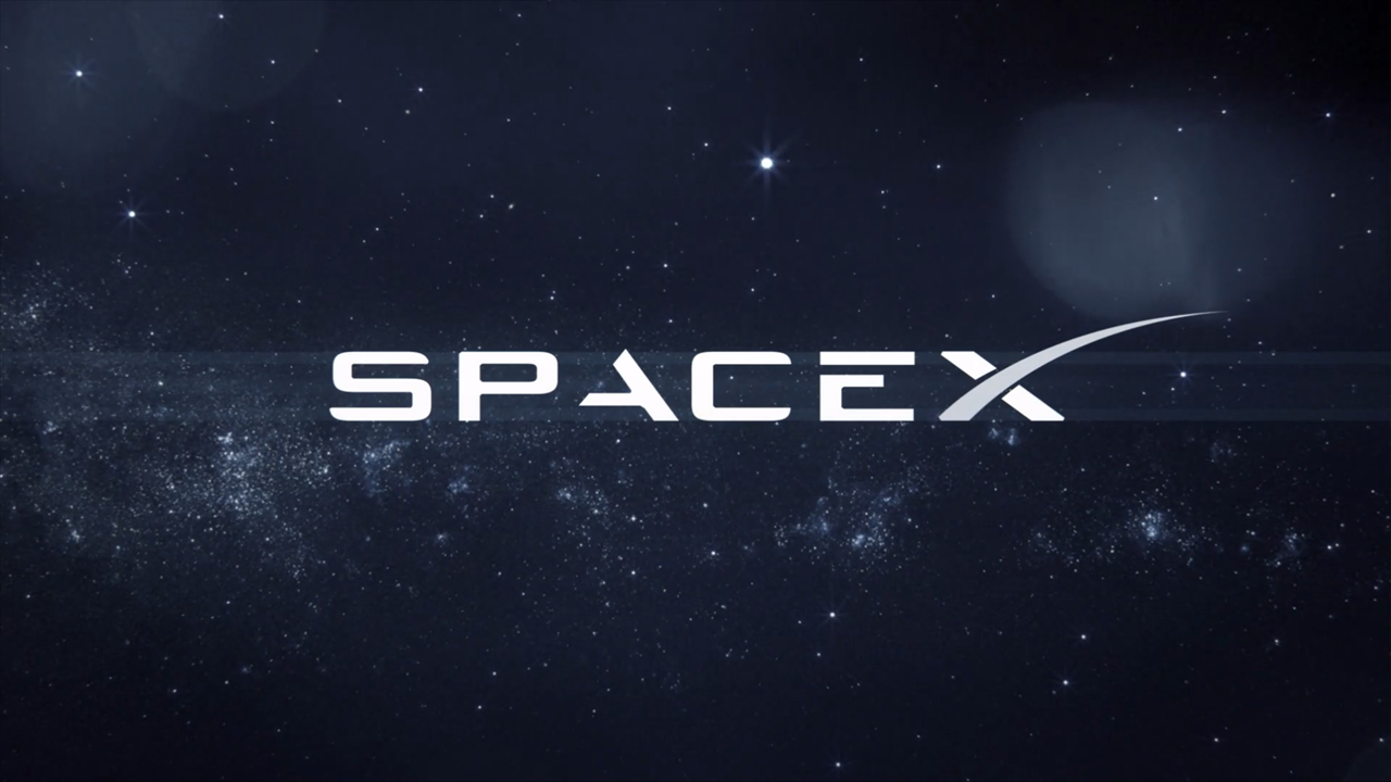 Imagem mostrando o logotipo da SpaceX, uma empresa aeroespacial americana, centralizado contra um fundo de estrelas e galáxias, sugerindo o espaço sideral. A palavra 'SpaceX' está escrita em letras maiúsculas brancas com um design futurista, destacada por uma linha curva que atravessa a letra 'X', simbolizando um foguete ou trajetória de voo. Esta imagem representa uma das líderes em exploração espacial e inovação tecnológica. Créditos: SpaceX.