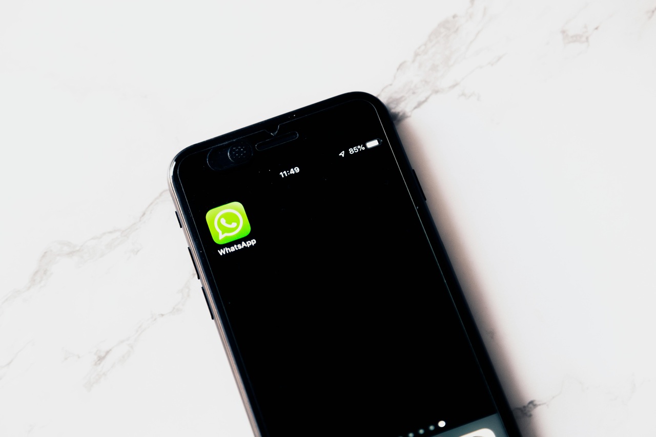 A imagem mostra um smartphone preto com a tela ligada, exibindo o ícone do aplicativo WhatsApp em destaque. O ícone do WhatsApp é verde com um símbolo de balão de fala branco. No topo da tela, é possível ver a hora 11:49 e o nível de bateria em 85%. O fundo da tela é preto, destacando ainda mais o ícone do aplicativo. A imagem é interessante e relevante porque destaca um dos aplicativos de mensagens mais populares do mundo, frequentemente usado para comunicação pessoal e profissional. Créditos: Image Hunter / Pexels