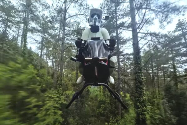 Star Wars? Volonaut lança moto voadora impressionante Um Stormtrooper de Star Wars pilota uma moto voadora futurista em uma floresta densa, cercado por árvores altas e vegetação exuberante. A moto exibe luzes na frente e parece flutuar no ar, criando um contraste marcante entre tecnologia e natureza. Créditos: Volonaut.