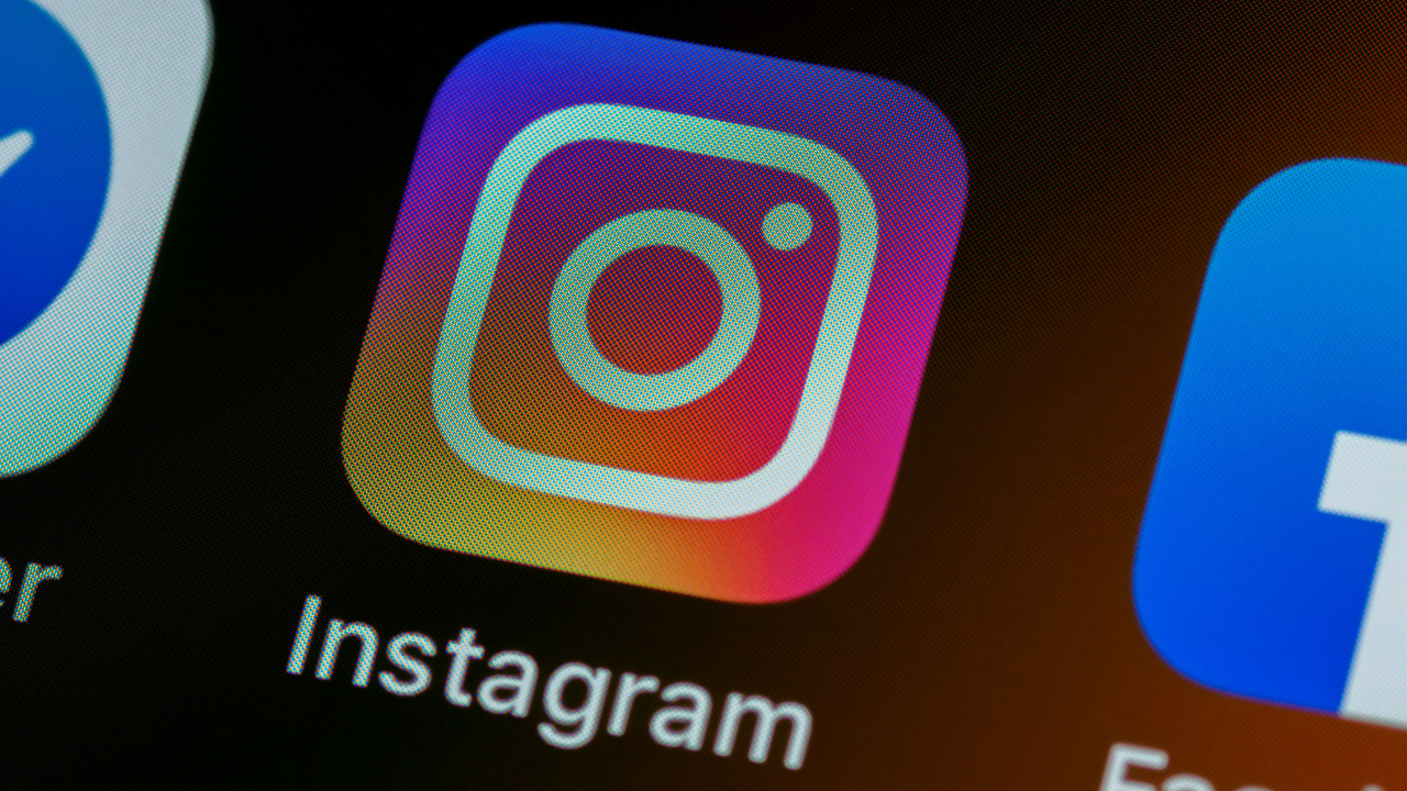 Ícone do aplicativo Instagram exibido em um dispositivo móvel. O ícone tem formato quadrado com bordas arredondadas e apresenta um gradiente vibrante do roxo ao laranja, com uma câmera estilizada ao centro. Abaixo, aparece o nome