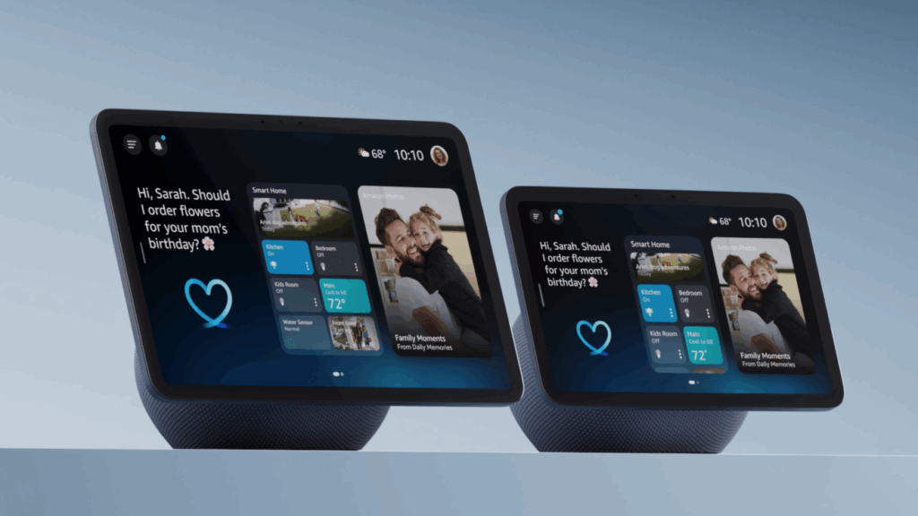 Dois dispositivos inteligentes Amazon Echo Show estão lado a lado sobre uma superfície plana com fundo azul claro. À direita, o Echo Show 8 exibe uma tela com informações personalizadas como previsão do tempo, controle de casa inteligente e um widget de fotos da família. À esquerda, o Echo Show 11 apresenta interface semelhante, com destaque para uma imagem diferente no widget de fotos. Ambos os dispositivos mostram a mensagem “Hi, Sarah. Should I order flowers for your mom’s birthday?”, evidenciando recursos de assistente pessoal e integração com o ambiente doméstico. Créditos: Amazon divulgação.