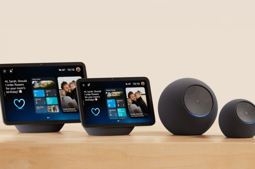 Conjunto dos novos dispositivos inteligentes da Amazon exibidos sobre uma superfície de madeira com fundo neutro. Inclui os modelos Echo Dot Max, Echo Studio (2ª geração), Echo Show 8 (4ª geração) e Echo Show 11, todos com design moderno e integração com Alexa+. Os displays inteligentes mostram informações personalizadas como previsão do tempo, eventos do calendário e uma mensagem interativa, enquanto os alto-falantes esféricos exibem um anel azul iluminado indicando atividade. Créditos: Amazon divulgação.