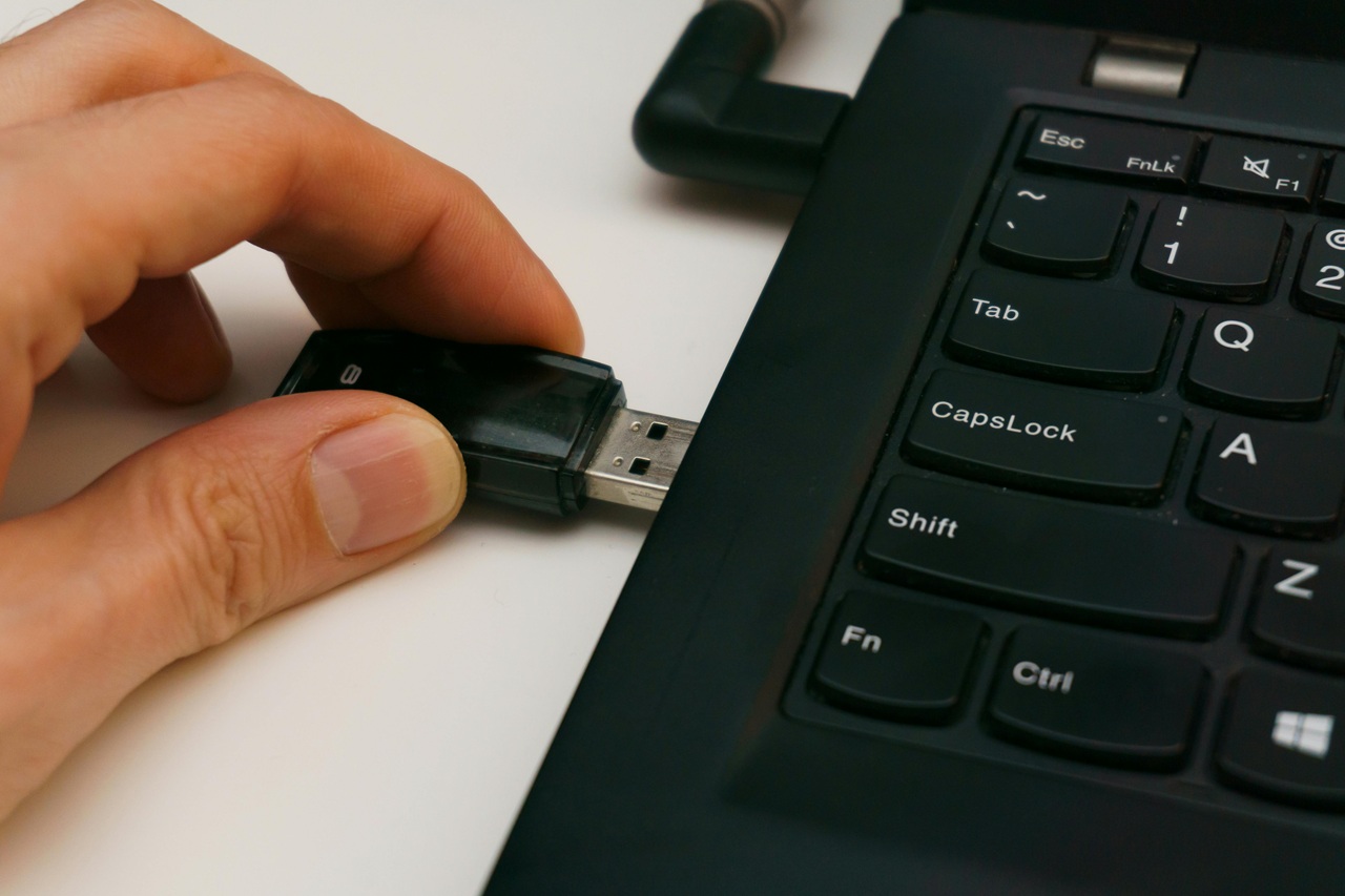 Pessoa conectando um pendrive USB em um notebook, representando processos de formatação de computadores, criação de mídia bootável, instalação do Windows, recuperação de sistema e uso de ferramentas para reinstalação do sistema operacional. Créditos: Aleksander Dumała - Pexels.