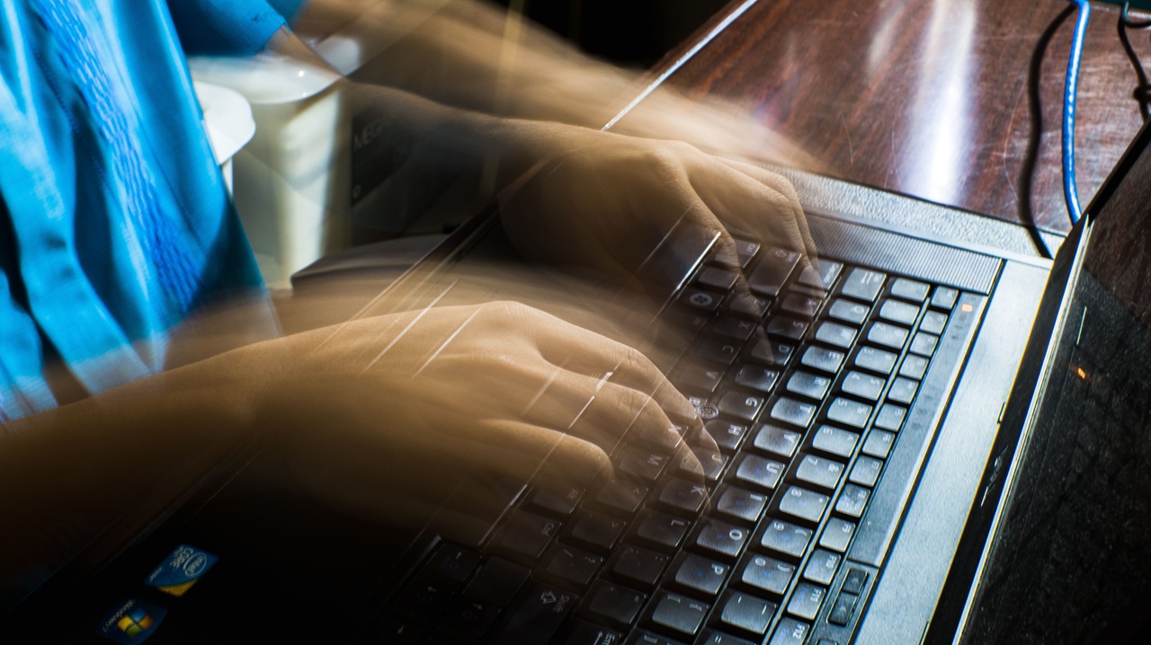 Mãos digitando rapidamente em um notebook, com efeito de movimento que representa atividades de informática, programação, cibersegurança ou ataques virtuais, ilustrando temas relacionados a golpes digitais, hackers e segurança da informação. Créditos: imagem de Nothing Ahead / Pexels.