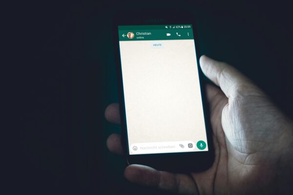 Pessoa segurando um smartphone com uma conversa aberta no WhatsApp, exibindo a interface de uma chamada de conversa e o campo para enviar mensagens. Créditos: Christian Wiediger / Unsplash
