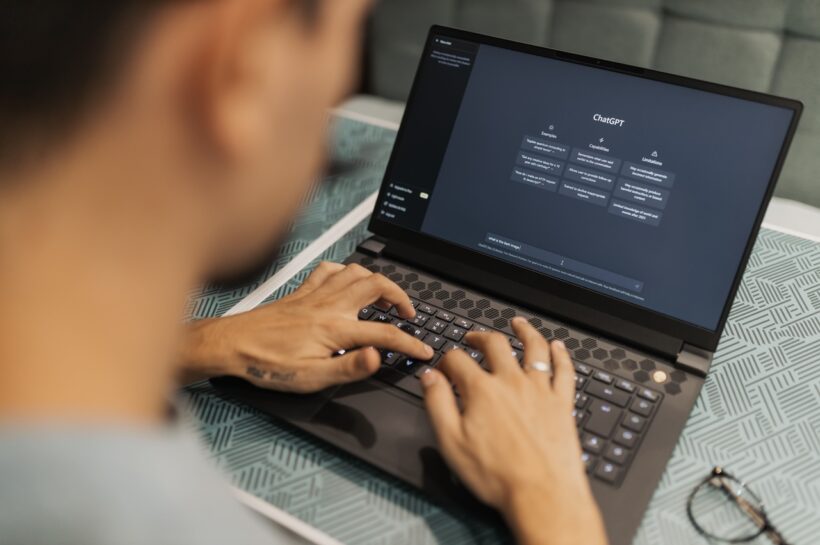 Pessoa usando um notebook com o ChatGPT aberto na tela, digitando uma mensagem no teclado. A interface do ChatGPT aparece em modo escuro. Créditos: Matheus Bertelli / Pexels.