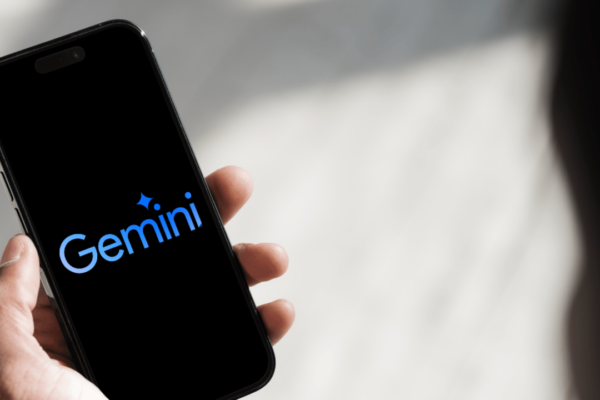 Mão segurando um smartphone com a tela preta exibindo o logotipo azul do Google Gemini, assistente de inteligência artificial do Google.