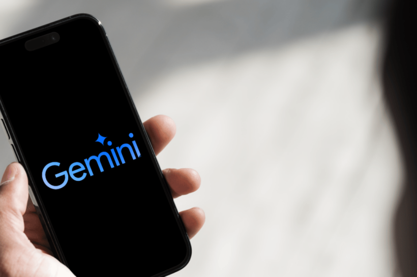 Mão segurando um smartphone com a tela preta exibindo o logotipo azul do Google Gemini, assistente de inteligência artificial do Google.